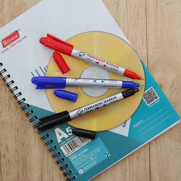 Bộ ba bút lông dầu FlexOffice FO-PM-01 màu đỏ, xanh và đen đặt trên đĩa CD và cuốn sổ tay A5.