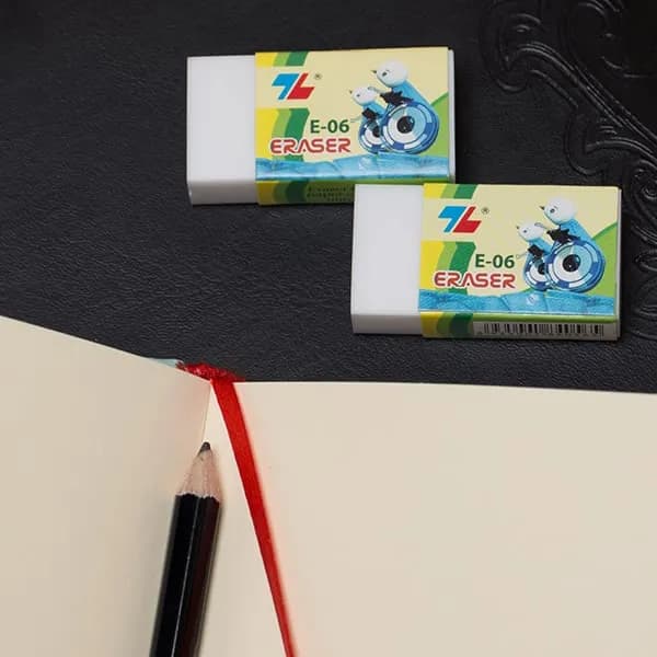 Hai cục gôm tẩy xóa chì Thiên Long E-06 đặt cạnh sổ tay có đánh dấu trang màu đỏ và bút chì đen