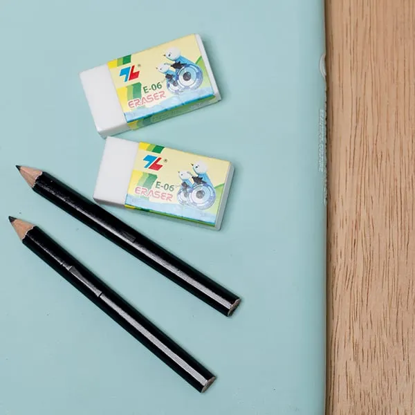 Hai cục gôm tẩy xóa chì thiên long e-06 nằm cạnh hai cây bút chì đen trên nền xanh nhạt