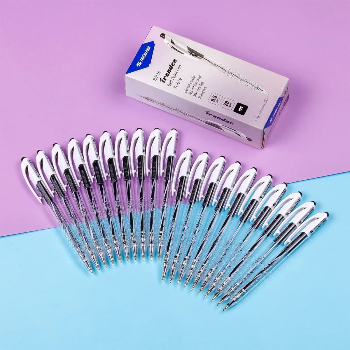 Hộp bút bi Thiên Long TL-079 0.5mm cùng các cây bút được xếp xòe trên nền hai màu tím và xanh.