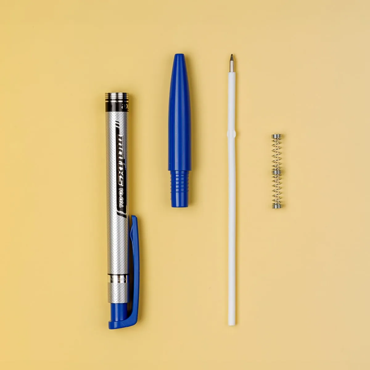 Các bộ phận của bút bi Flexoffice FO-024 được tháo rời gồm vỏ, nắp, ruột bút và lò xo trên nền vàng