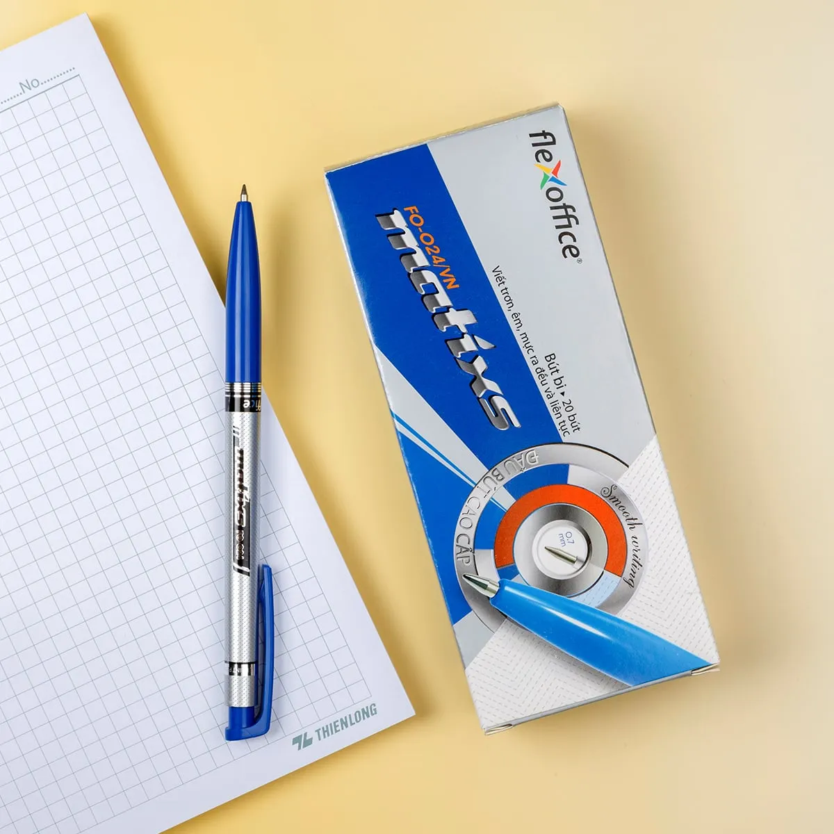 Bút bi Flexoffice FO-024 0.7mm màu xanh đặt cạnh hộp bút trên nền giấy ô ly.