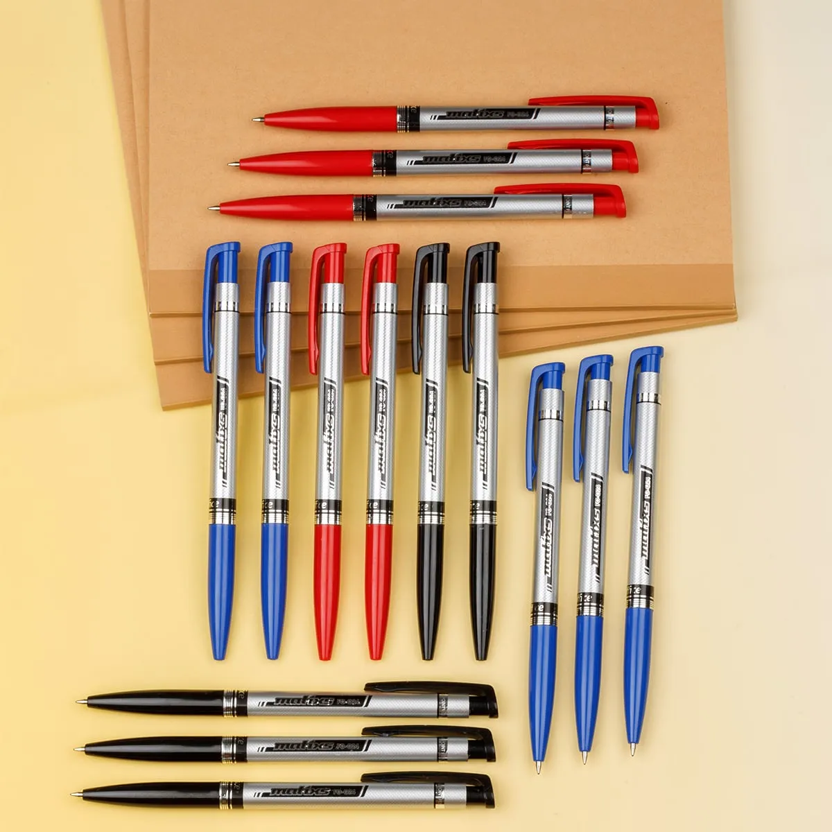 Các loại bút bi Flexoffice đa dạng màu sắc với thiết kế thân bạc hiện đại, sắp xếp trên nền giấy tập nâu.