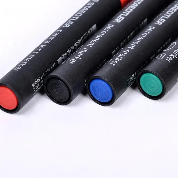 Bốn chiếc bút dạ dầu Staedtler với nắp đậy màu đỏ, đen, xanh dương và xanh lá cây được xếp cạnh nhau.