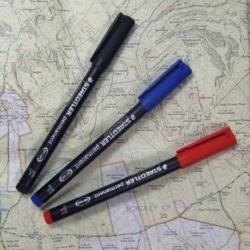 Ba chiếc bút dạ kính Staedtler với ba màu mực đen, xanh dương và đỏ đặt trên nền bản đồ địa hình.
