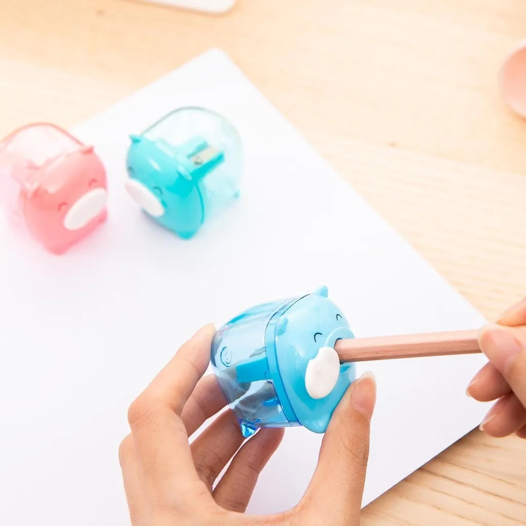 Tay người đang dùng gọt chì Deli hình con heo màu xanh để chuốt bút chì trên nền giấy trắng