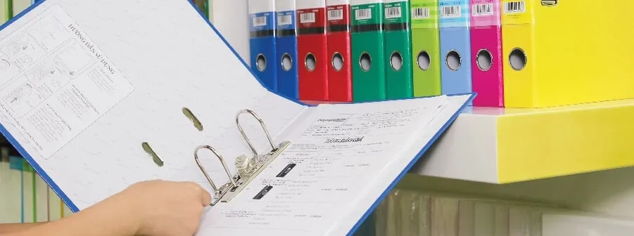 Người dùng đang thao tác mở file còng bật Flexoffice với các giấy tờ bên trong, phía sau là hàng loạt bìa hồ sơ màu sắc