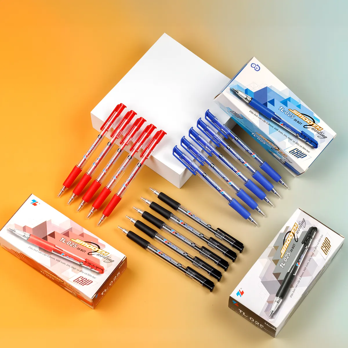 bút bi thiên long tl-025 với các phiên bản mực đỏ, xanh và đen cùng hộp đựng đặt trên nền màu vàng nhạt.